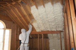 Installer installing white spray foam insulation onto ceiling in new construction building